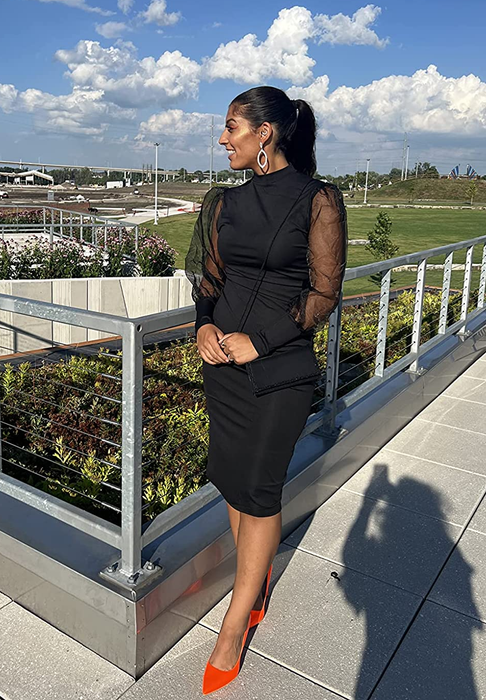 A reviewer wearing a black midi bodycon dress with mesh puffy lantern sleeves and red flats, standing outside in front of a field.