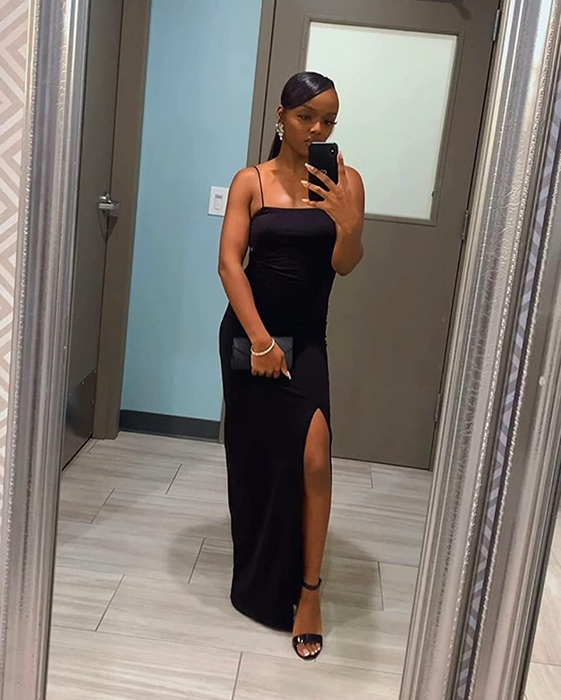 A reviewer wearing a black maxi bodycon dress with a side slit and spaghetti straps in front of a gray mirror.