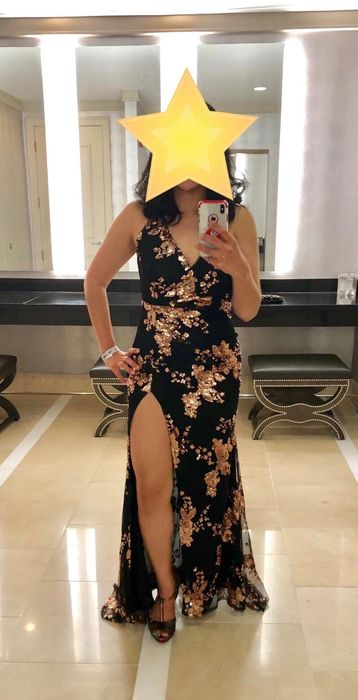 A reviewer showcasing the product in black with glittery floral details, paired with black open-toed heels, in front of a black counter.