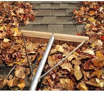 A roof brush being used to sweep leaves off a roof.