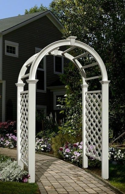 A white garden arbor featuring trellises on both sides, placed in a garden