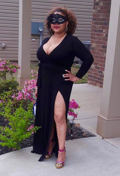 A reviewer modeling the product in front of flowers, wearing a black mask and pink strappy heels.
