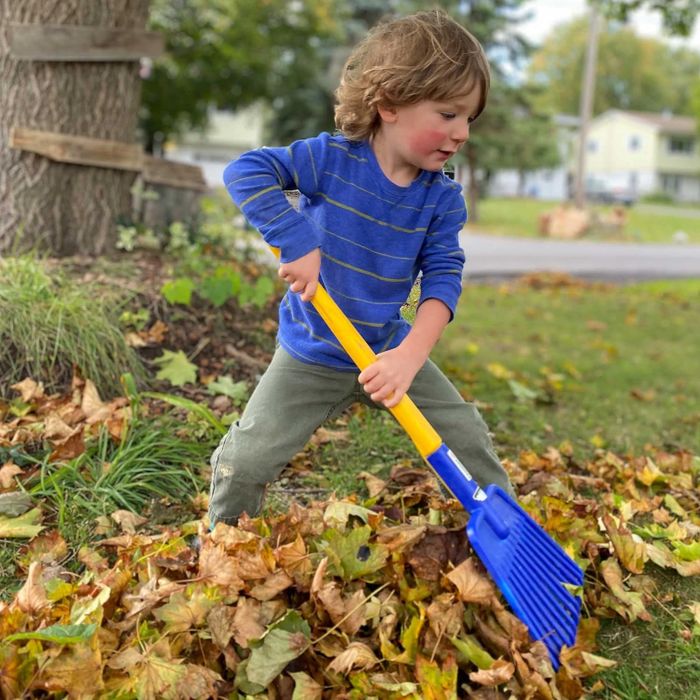 A child using a small blue rake designed for kids.