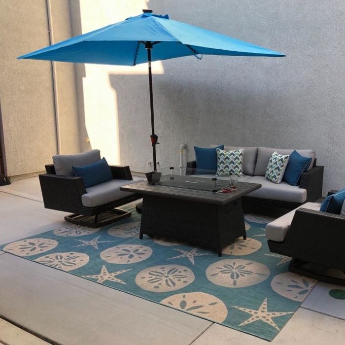 A reviewer's photo of a patio couch and chair set placed on a blue outdoor rug adorned with a shell print.