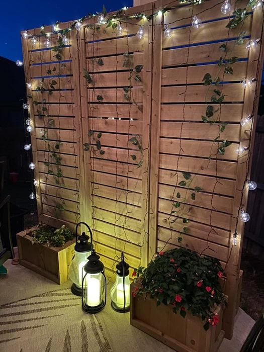 Vines and string lights hanging from a privacy screen, with lanterns in front of it.