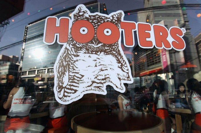 The Hooters restaurant window with the iconic owl logo, reflecting the city skyline and customers inside