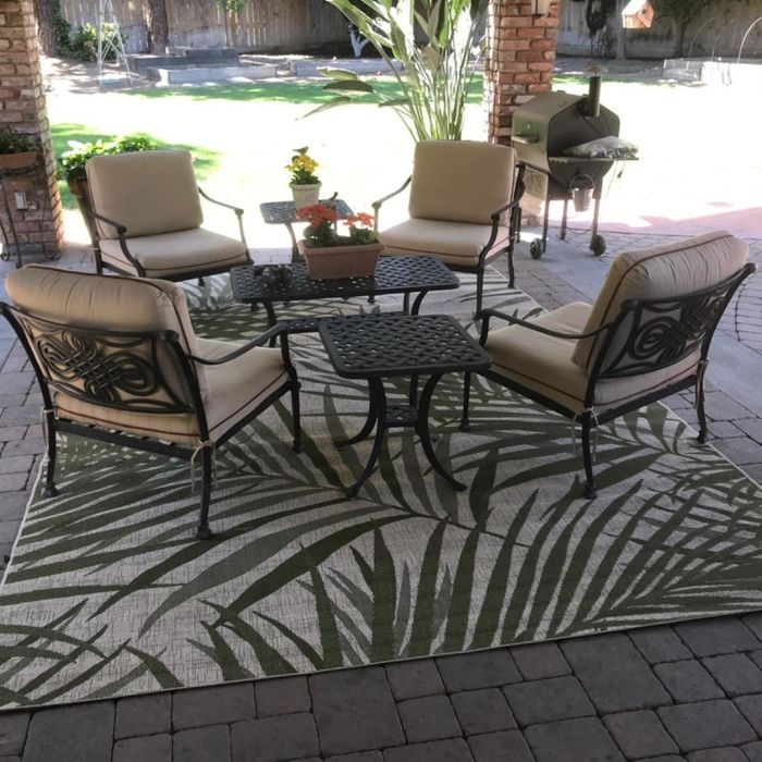 A reviewer's photo showing four chairs around a table on a patio, with a rug featuring a palm print underneath.