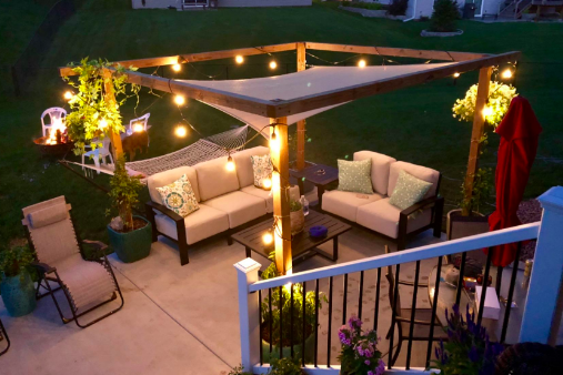 The reviewer’s backyard at night, featuring a canopy above a wooden frame, adorned with twinkling lights to create a cozy, magical atmosphere.