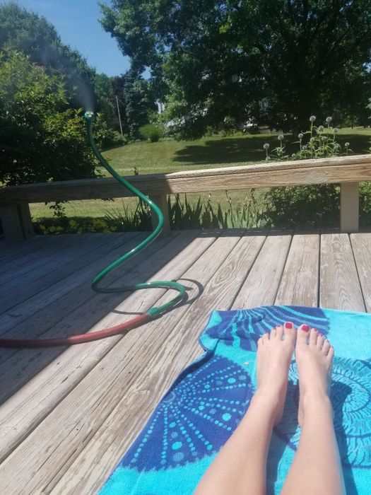 A green mister placed outside, with someone enjoying the sun while sunbathing.