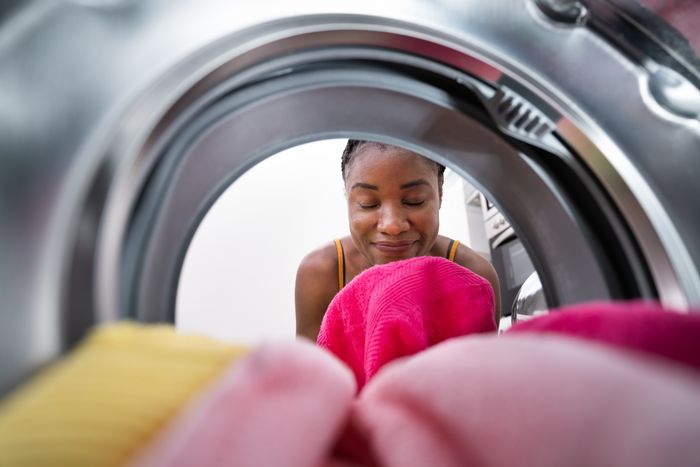 A person smiles as they look at the laundry inside an open washing machine, conveying a sense of satisfaction or contentment with the task at hand.