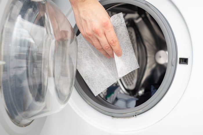 A hand is shown inserting a dryer sheet into an open washing machine, offering a demonstration of tips for maintaining laundry freshness.