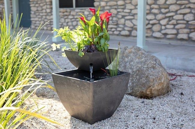 The water garden fountain, adorned with calla lilies, rests in the outdoor space with its upper tier beautifully displaying the flowers.