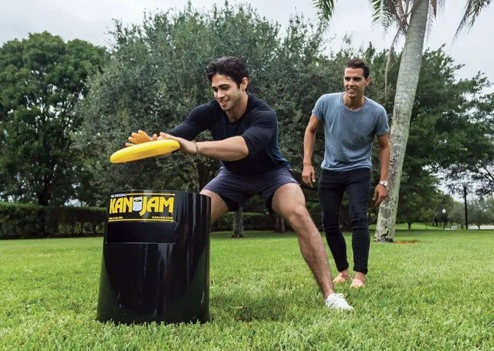 A model tossing a yellow frisbee into a black Kan Jam bin.