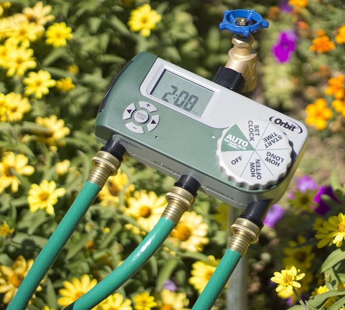 Three hoses connected to the timer, surrounded by blooming flowers.