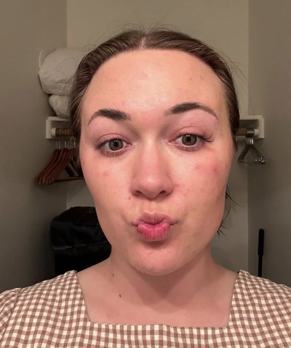 A person in a plaid shirt puckers their lips for a selfie, with clothing hangers and accessories visible behind them