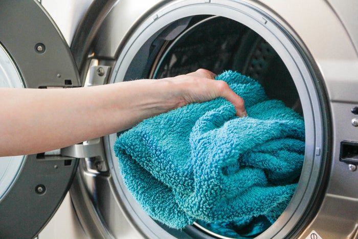 A person carefully placing a towel into a washing machine, demonstrating a common household task.