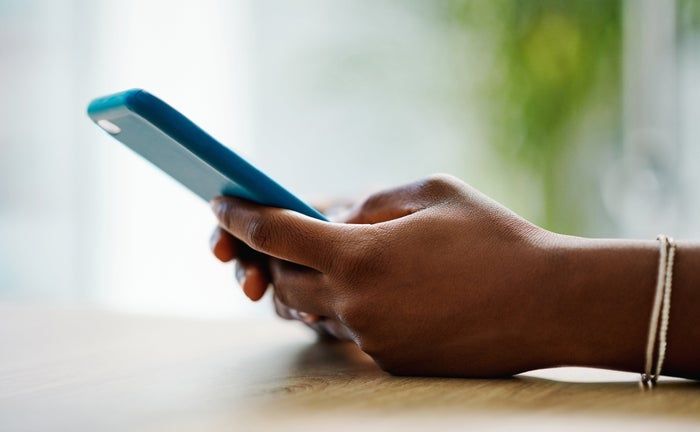 A person holding a smartphone with both hands, intently gazing at the screen. The background is softly blurred, drawing attention to the phone.
