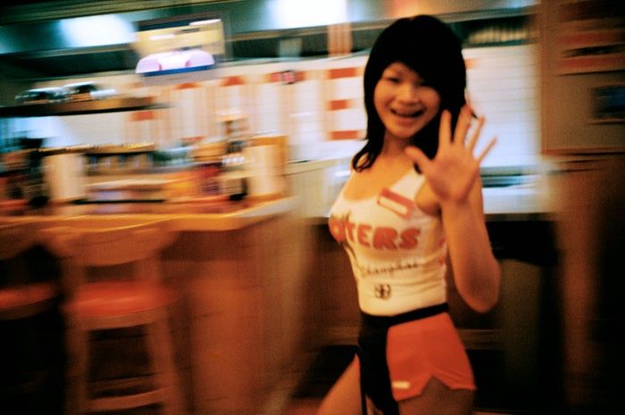 A person in Hooters attire waving while walking through a restaurant environment