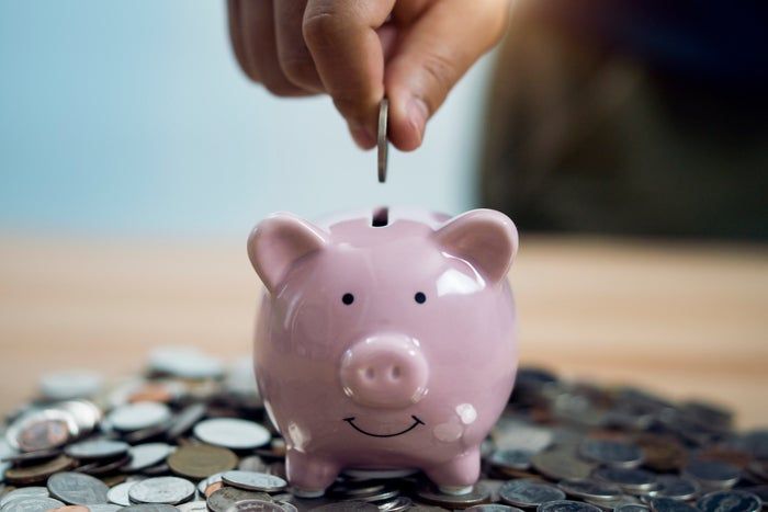 A hand gently placing a coin into a cheerful piggy bank, surrounded by scattered coins on a table.