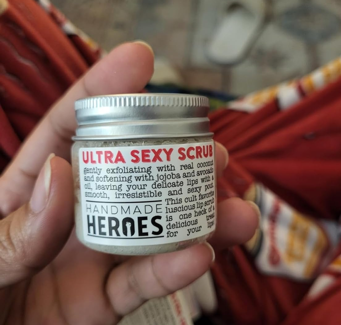A hand holding the jar of Handmade Heroes' Ultra Sexy Scrub, with product details, set in a relaxed environment.