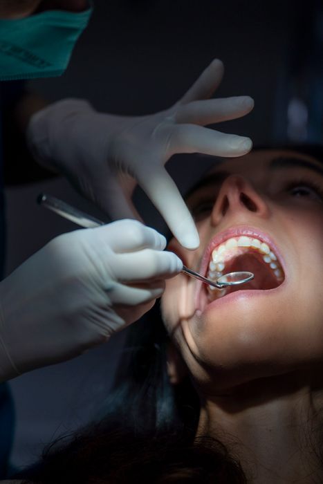 Person undergoing dental examination, dental tools in use. Dentist is wearing gloves and a mask