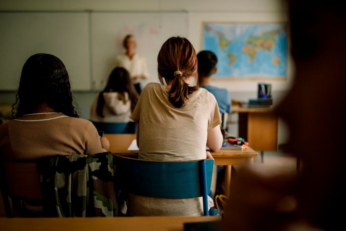 Students sitting in a classroom, listening to a teacher with a world map on the wall.
