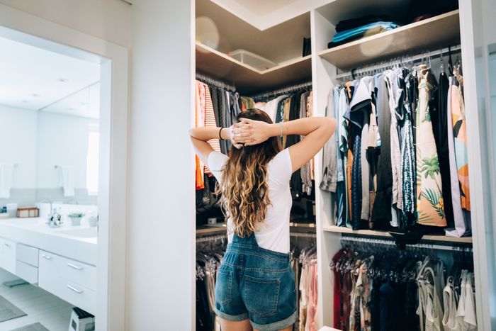 A person standing, hands on their head, gazing at a well-organized wardrobe in a bright, modern room.