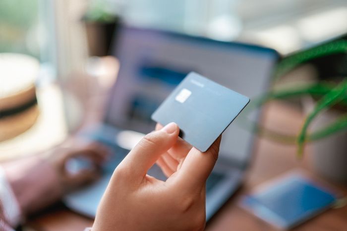 A person holding a credit card close to a laptop, possibly engaged in online shopping.