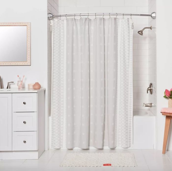 A round silver shower curtain rod installed in a bathroom with a white and gray shower curtain hanging.