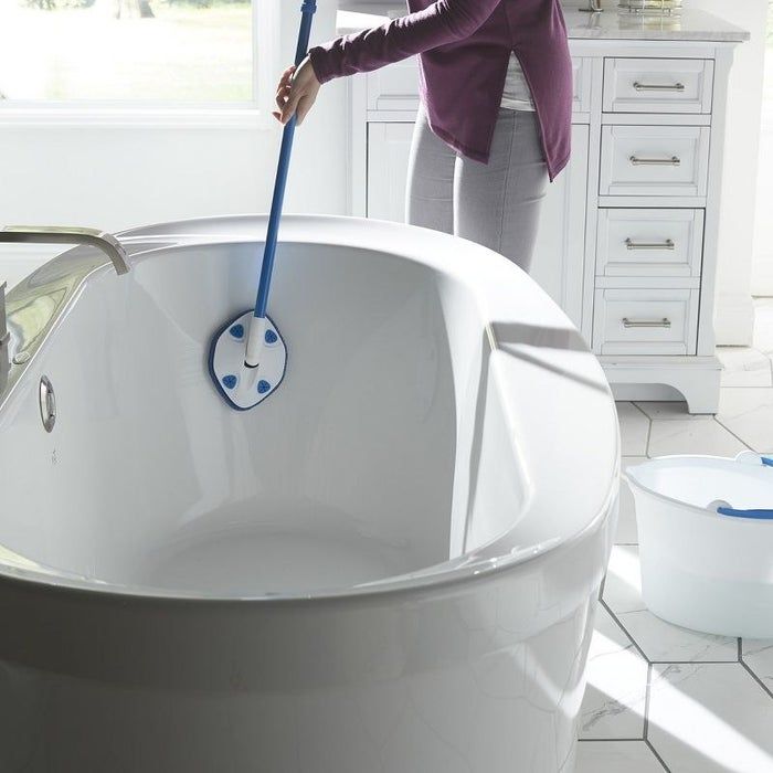 A person using a blue extendable Clorox tub cleaning wand to scrub a white porcelain bathtub.