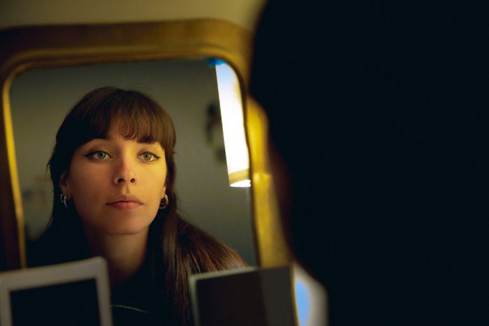 A person with straight hair and hoop earrings gazing into their reflection in a mirror.