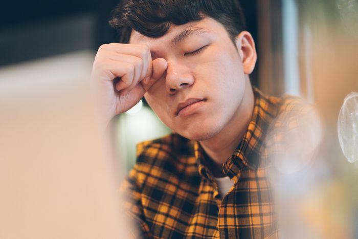 A person in a plaid shirt, eyes shut, rubbing their forehead, looking overwhelmed and exhausted.