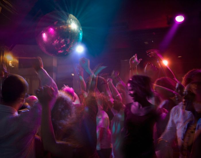 A lively nightclub scene with people dancing energetically beneath a sparkling disco ball