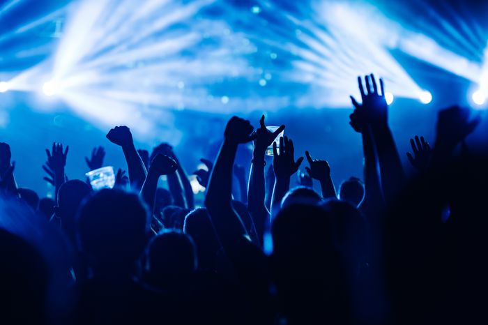 A vibrant crowd at a concert, hands raised in the air, bathed in the bright glow of stage lights, capturing the excitement and energy of the live music experience.