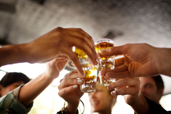 A group of people raising their shot glasses for a celebratory toast indoors.