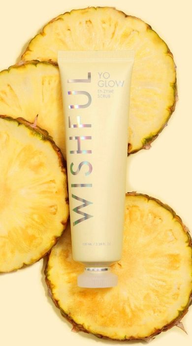Tube of Wishful Yo Glow Enzyme Scrub surrounded by fresh pineapple slices.