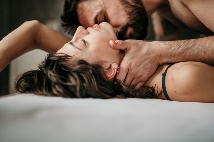 Two people lying in bed, holding each other closely. One gently cradles the other's head, eyes closed, conveying a sense of intimacy and affection.