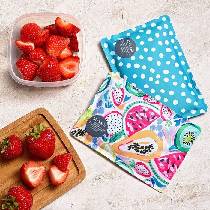 Reusable snack bags featuring vibrant fruit and polka dot patterns, accompanied by chopped strawberries in a plastic container and on a cutting board