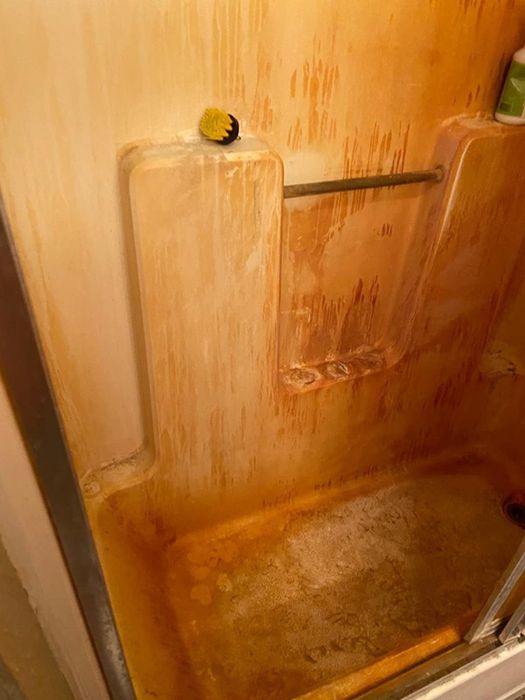 A reviewer's tub and shower walls covered in orange stains before using the hard-water stain remover