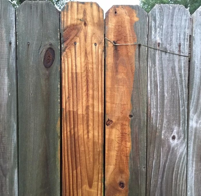 A wooden fence that's brown in the center from where it's been pressure washed, with gray residue still visible on either side
