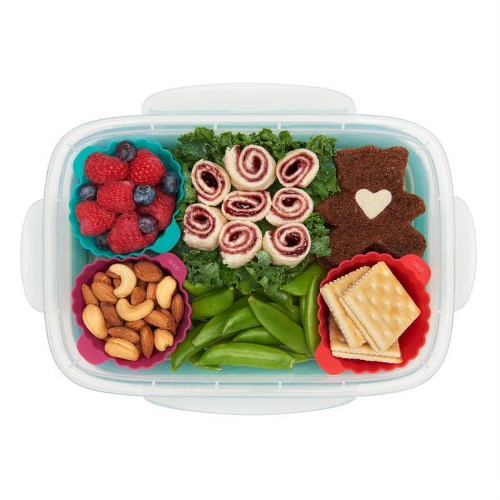 A lunchbox filled with rolled sandwiches, a bear-shaped snack, snap peas, mixed berries, crackers, and nuts neatly arranged in silicone containers