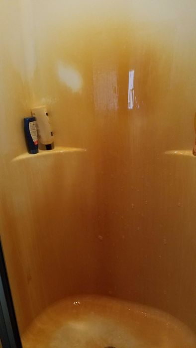 A photo showing a white shower with dark orange rust stains, stretching from the floor to the top of the wall.