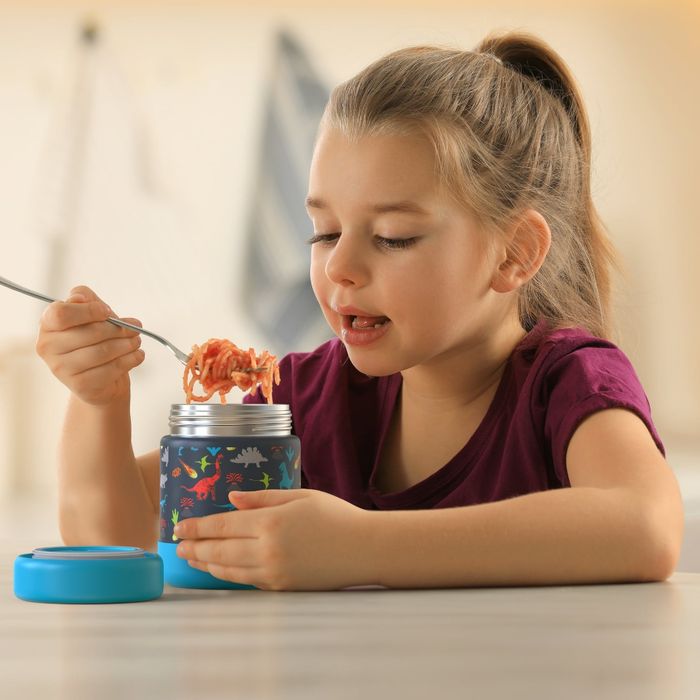 A casually dressed child enjoying noodles from a dinosaur-themed thermal container