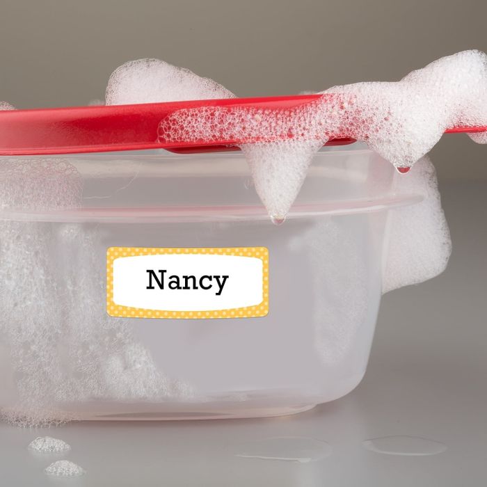 A plastic container labeled "Nancy" with soapy foam spilling out from its red lid
