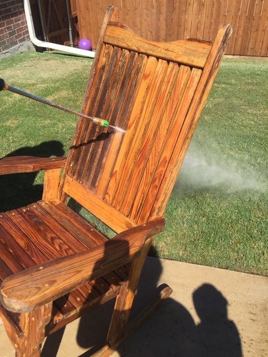 An outdoor wooden rocker being pressure washed, showing one side with dark stains and the other side looking as good as new
