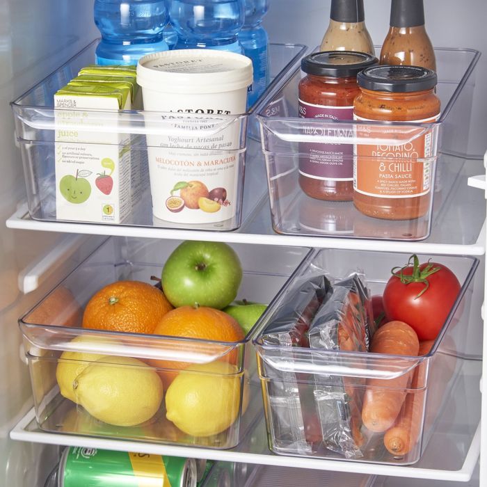 A neatly organized refrigerator featuring clear bins filled with bottled water, juice boxes, sauce jars, and an assortment of fruits and vegetables like lemons, apples, carrots, and tomatoes.
