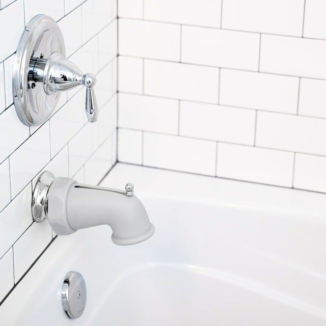Bathroom featuring white tiles, a silver bathtub faucet, and shower controls