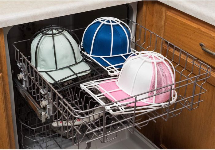 Baseball caps are cleaned in a dishwasher, where they rest on a rack supported by a plastic frame to prevent any harm during the washing process.