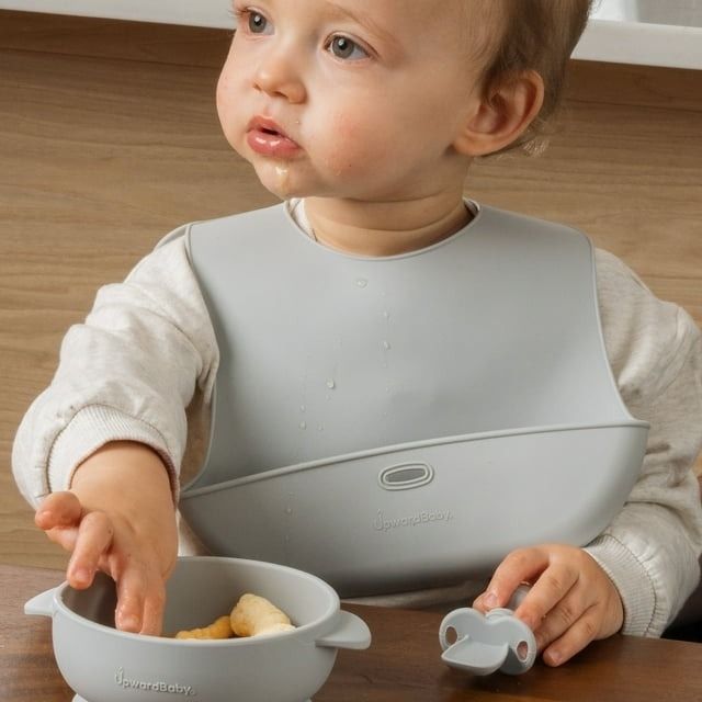 Toddler wearing a bib, holding a bowl and utensil, with a silicone suction product in view