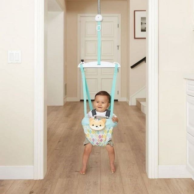 A toddler happily playing in a doorway jumper, wearing a cute romper with a bow tie.